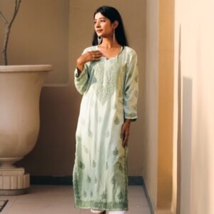 South Asian woman in traditional pistachio green chikankari kurti, enjoying a serene moment indoors.
